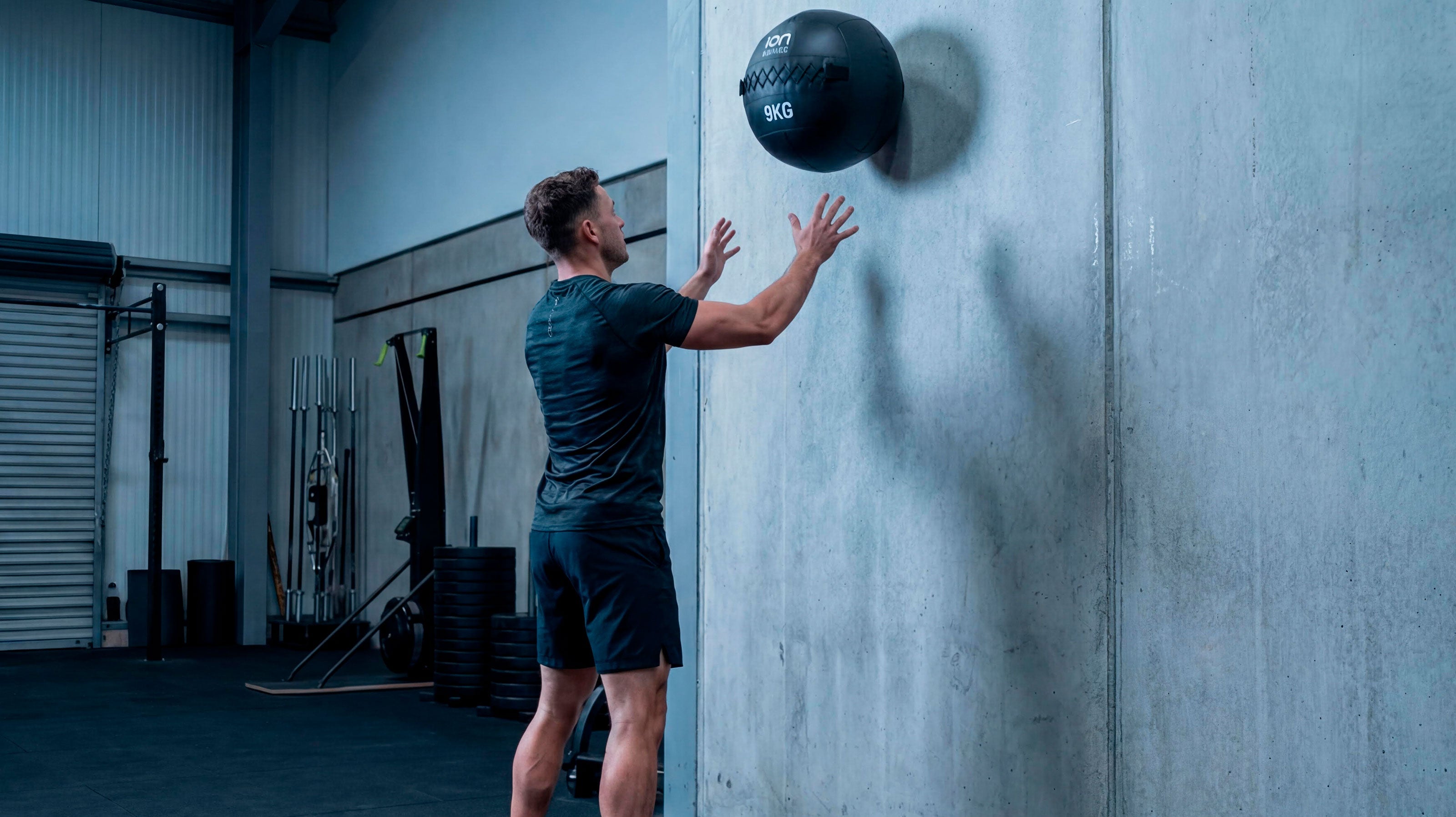 Un hombre lanza un balón medicinal hacia arriba contra una pared, en un ejercicio de crossfit para entrenar la fuerza explosiva.